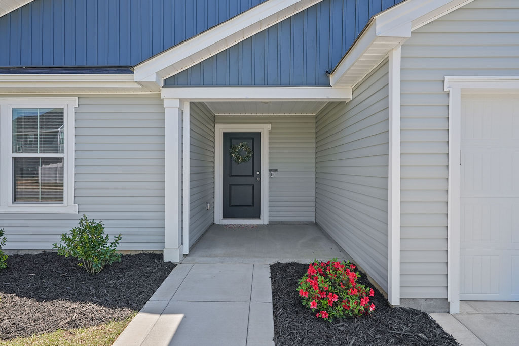 Covered front porch entry of single-story home in Raeford NC near Fort Bragg with dark front door, white trim, and landscaped flower beds