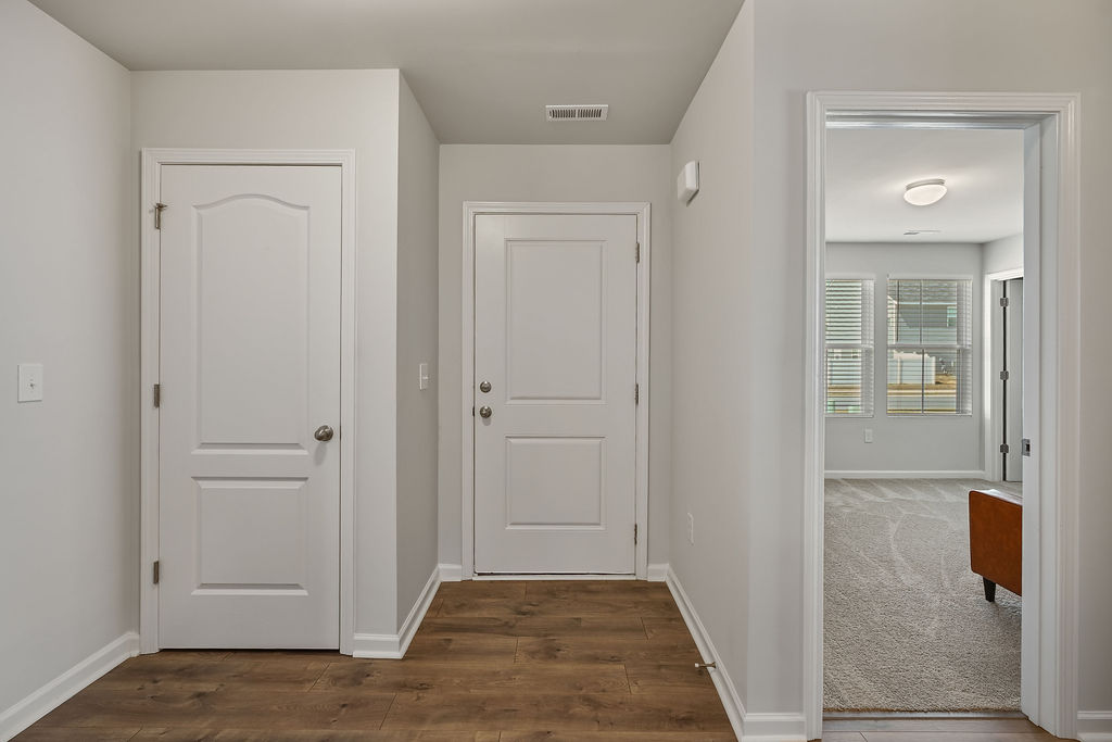 Interior entry hallway of 2024-built home in Raeford NC with laminate flooring, white interior doors, and view into carpeted room
