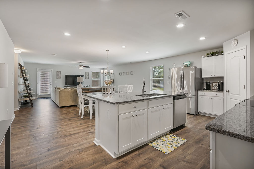 Open-concept kitchen with granite island, white cabinets, stainless steel appliances, and laminate flooring opening to dining and living area in Kirwin Village home near Fort Bragg