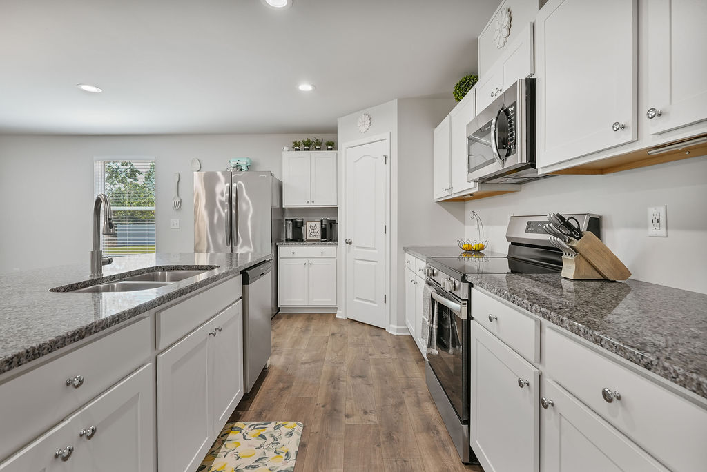 Kitchen with granite countertops, white shaker cabinets, stainless steel range, microwave, and refrigerator in 2024-built home at 250 Melbourne Dr, Raeford NC