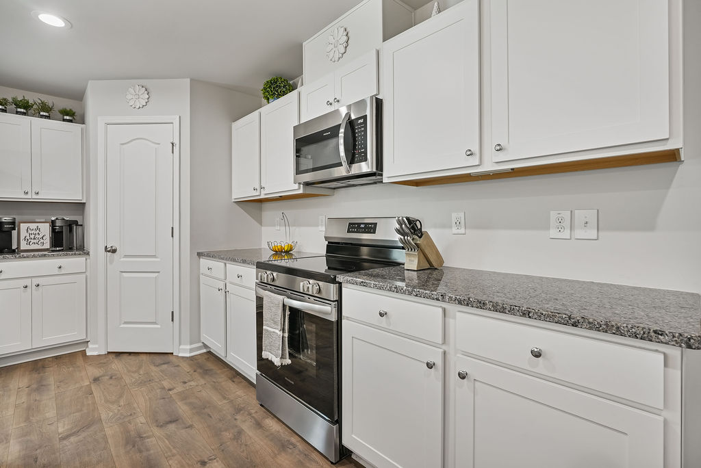 White kitchen cabinetry with granite countertops, stainless steel range and microwave, and laminate flooring in single-story home near Fort Bragg in Raeford NC