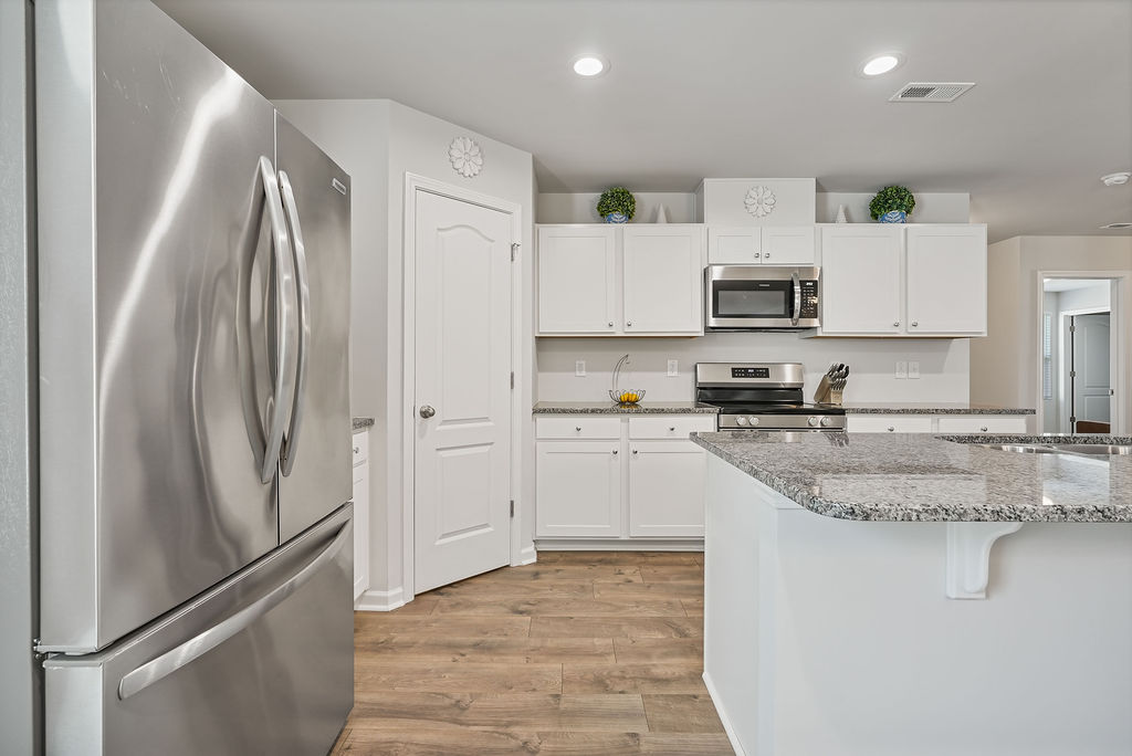 Stainless steel refrigerator and granite kitchen island with white cabinetry in 2024-built home in Kirwin Village, Raeford NC