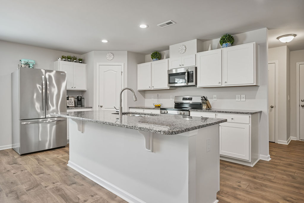 Full view of granite kitchen island with sink, white cabinetry, and stainless steel appliances in open-concept kitchen at 250 Melbourne Dr, Raeford NC