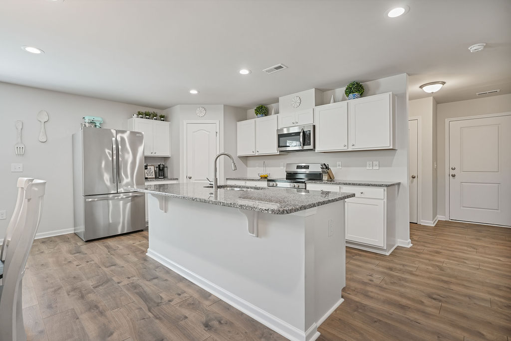 Wide view of white kitchen with granite island, stainless steel appliances, recessed lighting, and laminate flooring in 2024-built single-story home near Fort Bragg