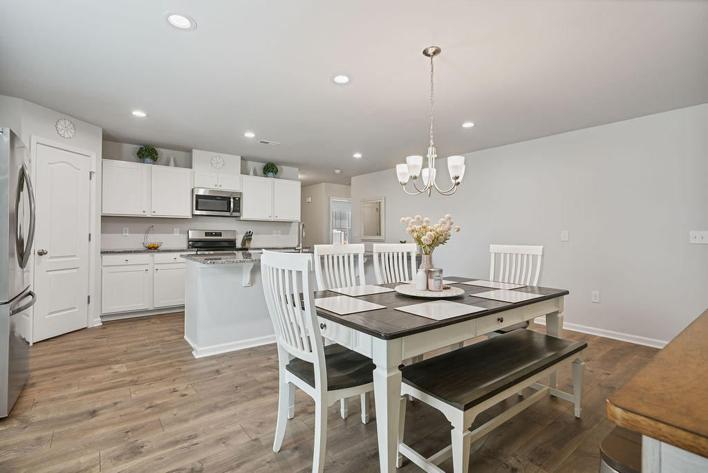 Dining area with pendant chandelier and view of open kitchen with white cabinets, granite island, and stainless appliances in 2024-built home in Kirwin Village, Raeford NC