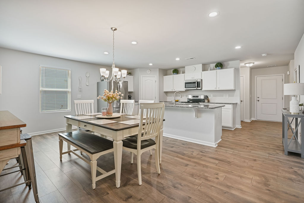 Wide view of open dining and kitchen area with laminate flooring, white cabinetry, granite island, stainless steel appliances, and recessed lighting at 250 Melbourne Dr, Raeford NC