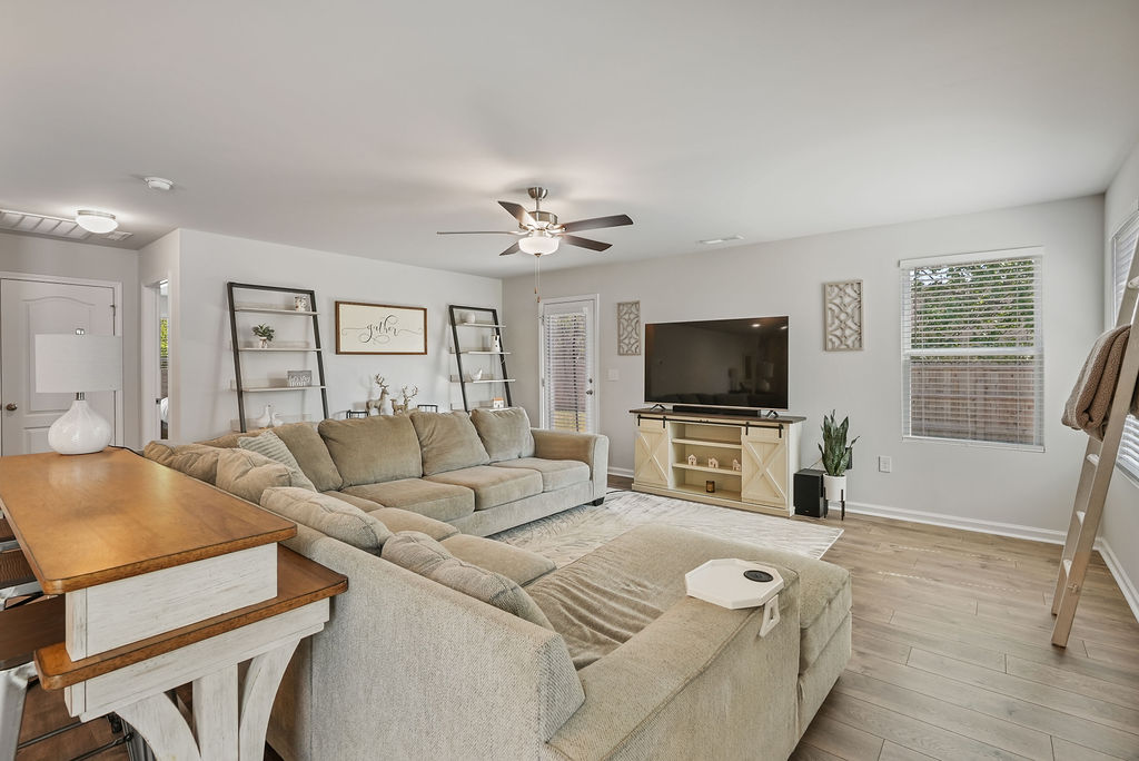 Spacious living room with ceiling fan, laminate flooring, and natural light from multiple windows in 2024-built home in Kirwin Village, Raeford NC