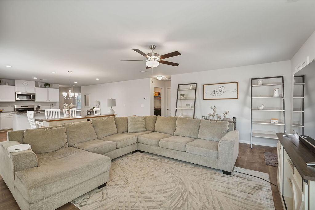 Open-concept living room with ceiling fan and full view through to kitchen with white cabinets and granite island in single-story home near Fort Bragg in Raeford NC