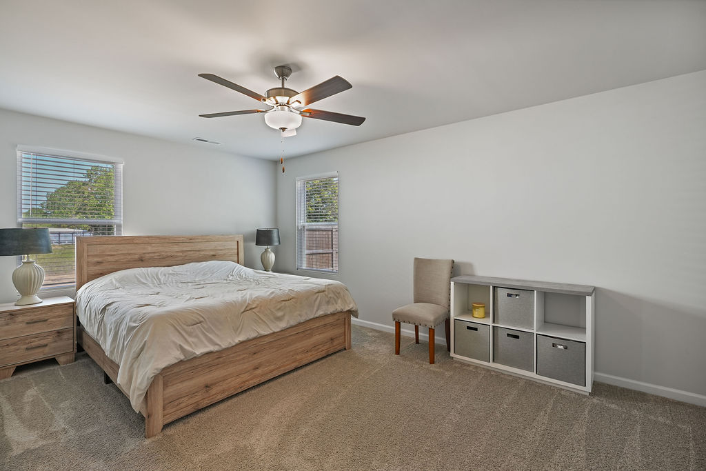 Carpeted primary bedroom with ceiling fan, two windows with natural light, and generous floor space in 2024-built home near Fort Bragg in Raeford NC